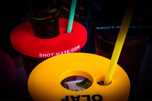 Mehrere Booze Dock Aufsätze in Gelb, Rot und Schwarz mit eingesetzten Flaschen und Strohhalmen auf Gläsern.