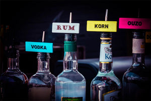 Flaschen mit bunten Shot-Mate-Clips zur Kennzeichnung von Spirituosen wie Vodka, Rum, Korn und Ouzo.