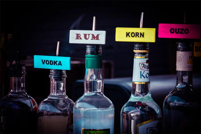 Flaschen mit bunten Shot-Mate-Clips zur Kennzeichnung von Spirituosen wie Vodka, Rum, Korn und Ouzo.