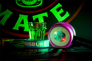 Leuchtender LED-Spinner, Shotglas mit grünem Drink und Silikonarmbänder vor Shot-Mate-Logo.