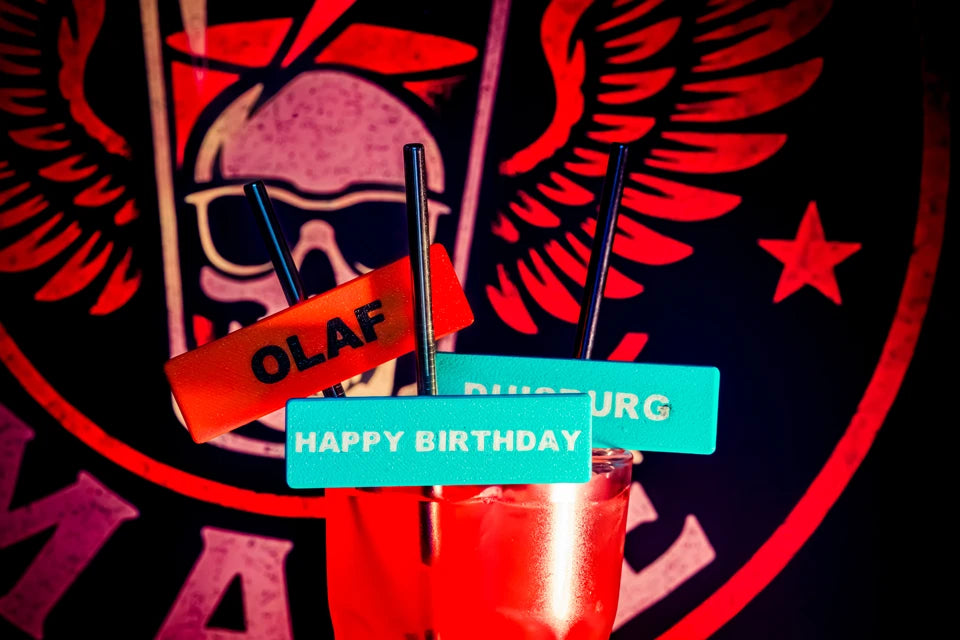 Personalisierte Shot-Mate Strohhalme mit den Aufschriften Olaf, Happy Birthday und Duisburg in einem Getränk. Individuelle Namensschilder helfen bei der Kennzeichnung von Getränken auf Partys und Veranstaltungen.