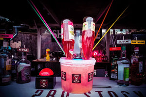 Shot-Mate Booze Pott Getränkespender mit mehreren Cocktailflaschen in einer Barumgebung. Das System eignet sich für Cocktails, Longdrinks, Partys und Veranstaltungen.