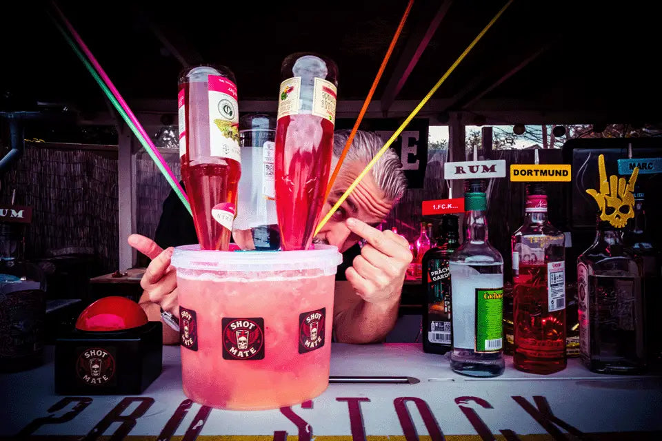 Person zeigt auf den Shot-Mate Booze Pott Getränkespender mit mehreren Cocktailflaschen. Das System eignet sich für Cocktails, Longdrinks, Partys und Veranstaltungen.